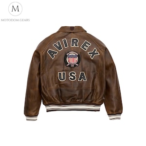 May include: Brown leather jacket with the word "AVIREX" arched across the back, above a patch with the American flag and the word "USA". The jacket has a collar and ribbed cuffs and hem.