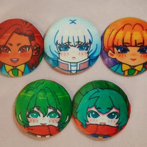 以下が含まれることがあります： アニメスタイルのキャラクターの肖像画が描かれた、丸いボタン5個セット。ボタンには、赤、青、緑など様々な髪色のキャラクターが描かれており、詳細な顔の特徴とカラフルな衣装が施されています。