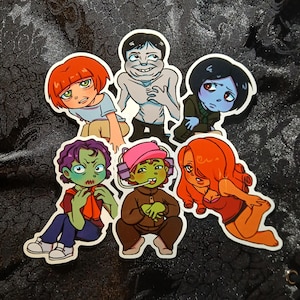Può includere: Una collezione di sei adesivi di cartoni animati con vari personaggi con design unici. Gli adesivi presentano una gamma di colori, tra cui rosso, blu, verde e marrone. I personaggi hanno espressioni facciali e abiti distinti.