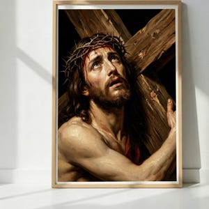 以下が含まれることがあります： 額縁に入った宗教画。長い茶色の髪、ひげ、いばらの冠をかぶった男性が描かれています。彼は木製の十字架を運び、悲しそうな表情をしています。アートワークは木製のフレームに入っています。