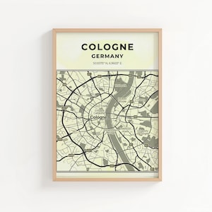 Puede incluir: Impresión enmarcada que presenta un mapa de Colonia, Alemania, con el nombre de la ciudad y las coordenadas en la parte superior. El mapa es en blanco y negro, con un fondo amarillo claro y un marco de madera.