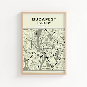 May include: A framed map print of Budapest, Hungary. The print features a detailed street map in black and grey, with the city name and coordinates at the top. The frame is a light wood colour.