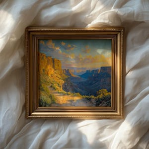 May include: A framed landscape painting of a canyon scene, with tall rock formations illuminated by sunlight. The artwork shows a path leading into the canyon, with a blue sky and clouds. The frame is gold-coloured.