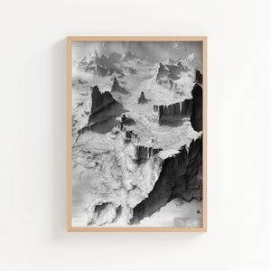 May include: Black and white landscape art print in a light wood frame. The print shows a detailed aerial view of a mountainous region with deep canyons and peaks. The artwork is a grayscale image with varying shades of grey.