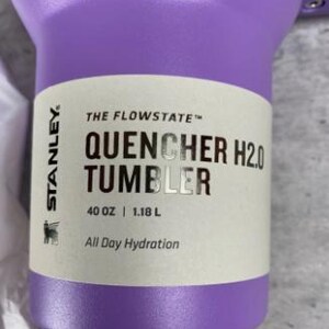 Op de afbeelding: Een paarse Stanley Quencher H2.0 Tumbler. De beker heeft een inhoud van 1,18 liter en is voorzien van de tekst "All Day Hydration". De beker is ontworpen voor hydratatie onderweg.