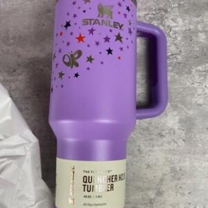 Op de afbeelding: Een paarse Stanley Quencher H2.0 tumbler met een handvat, versierd met sterren en een vlinder. De tumbler heeft een rietje en een capaciteit van 1,18L. De tekst "STANLEY" is zichtbaar.