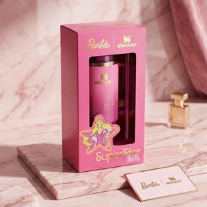 K&ouml;nnte beinhalten: Ein pinkfarbenes Stanley-Reisebecher- und Box-Set mit dem Barbie-Logo und einer Stern-Grafik. Auf der Box steht "Superstar Barbie" in goldfarbenen Buchstaben. Eine kleine Karte mit den Barbie- und Stanley-Logos ist ebenfalls zu sehen.