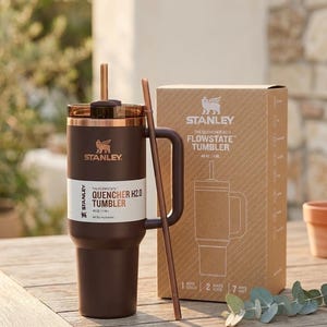 May include: A brown Stanley Quencher H2.0 Flowstate tumbler with a handle and straw, next to its cardboard box. The tumbler is 1.18L. The box shows the tumbler's design and the Stanley logo.