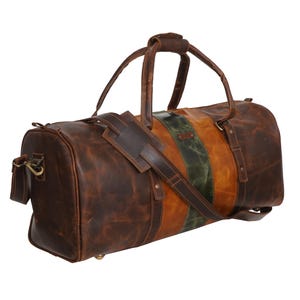 Pu&ograve; includere: Una borsa da viaggio in pelle marrone con tracolla e manici. La borsa presenta una striscia verticale in pelle verde e marrone. La borsa ha un aspetto invecchiato con cuciture e hardware in metallo visibili.