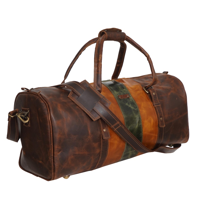 Pu&ograve; includere: Una borsa da viaggio in pelle marrone con tracolla e manici. La borsa presenta una striscia verticale in pelle verde e marrone. La borsa ha un aspetto invecchiato con cuciture e hardware in metallo visibili.