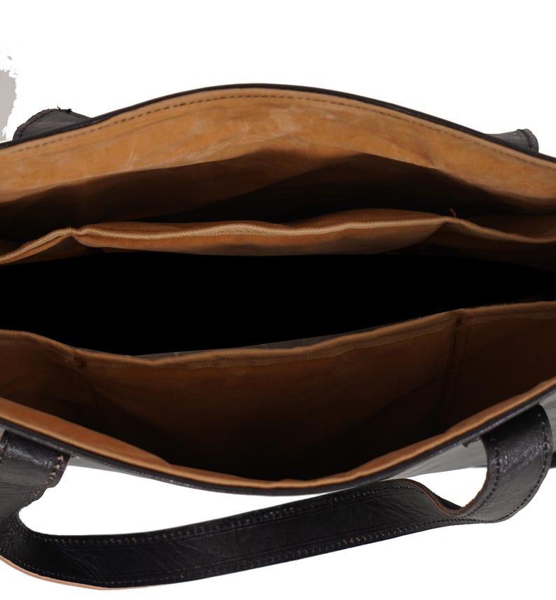 May include: Open view of a black leather tote bag with a light brown interior. The bag has multiple compartments and a structured design. The handles are also black leather. The bag appears to be empty.