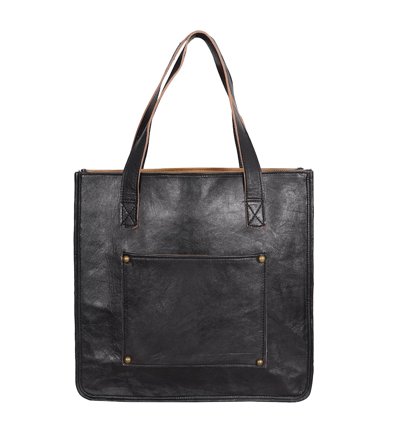 May include: Black leather tote bag with a rectangular shape and a front pocket. The bag has two brown leather handles and brass rivets. The interior is lined with a lighter brown material. A stylish and functional accessory.
