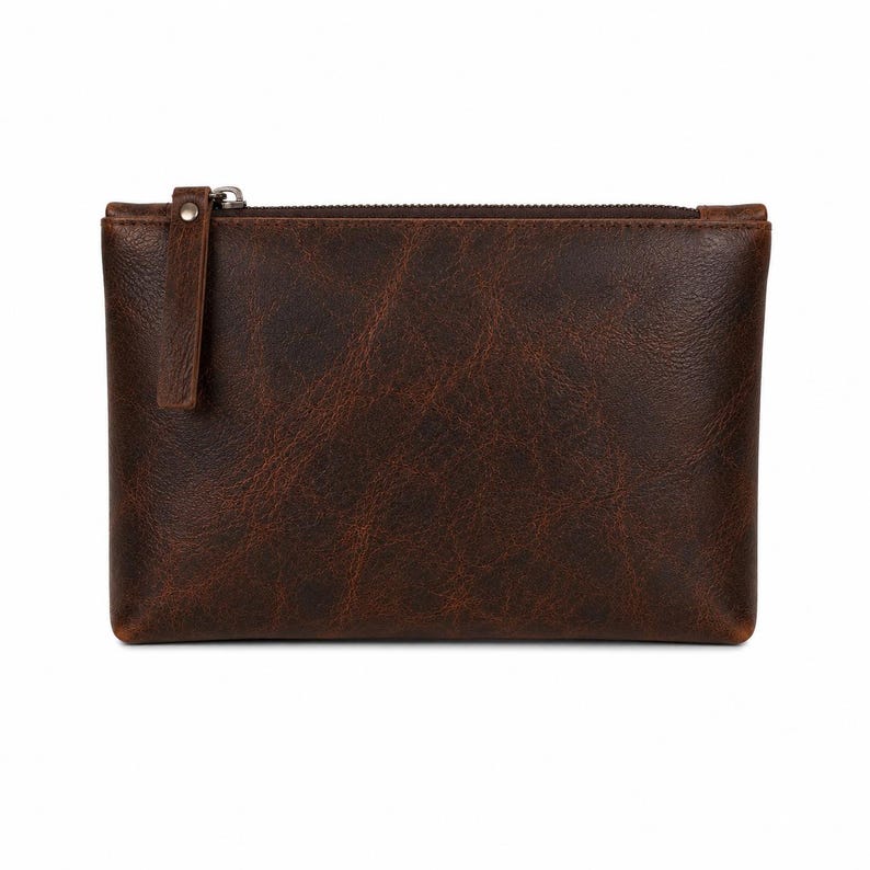 Pu&ograve; includere: Una pochette rettangolare in pelle marrone scuro con una texture a grana visibile, una chiusura a zip superiore e una linguetta in pelle abbinata fissata con un piccolo rivetto in metallo color argento. La pochette ha un design piatto.