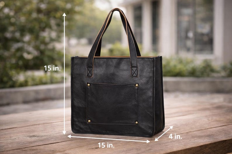 May include: Black leather tote bag with a rectangular shape, measuring 15 inches in height, 15 inches in width, and 4 inches in depth. Features a front pocket, gold-colored rivets, and two top handles. The bag is designed for carrying items.