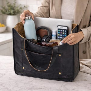 May include: A black leather tote bag with a light blue water bottle, laptop, headphones, phone, and other items inside. The bag has a large pocket on the front and is being held by a person wearing a tan coat.