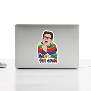 Könnte beinhalten: Ein Aufkleber mit einer Cartoon-Illustration einer Person mit Brille und einem gestreiften Pullover, die den Mittelfinger zeigt. Der Text "Suck my fat one!" steht darunter in bunten Buchstaben.
