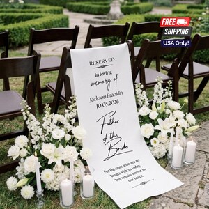 May include: A white memorial sign featuring black text that reads: RESERVED in loving memory of Jackson Franklin 10.05.2026 Father of the Bride For the ones who are no longer with us today, but remain forever in our hearts, displayed with white flowers.