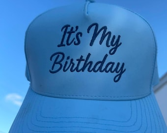 May include: Light blue trucker hat with the text "It's My Birthday" in dark blue script. The hat has a curved brim and a mesh back, perfect for a birthday celebration.