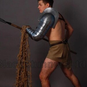 May include: A person in gladiator armour, including a metal arm guard and shoulder piece, holding a trident and a rope net. The person is wearing a brown skirt and is barefoot. The image has the text "BlackstunnersLtd" on the bottom.