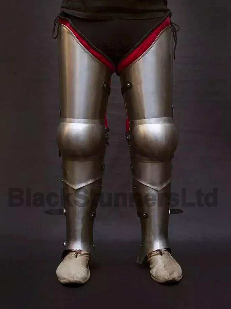 May include: Full leg armor made of polished metal, featuring articulated knee and shin plates. The armor is worn over black fabric with red trim. The image includes the text "BlackStunnersLtd".