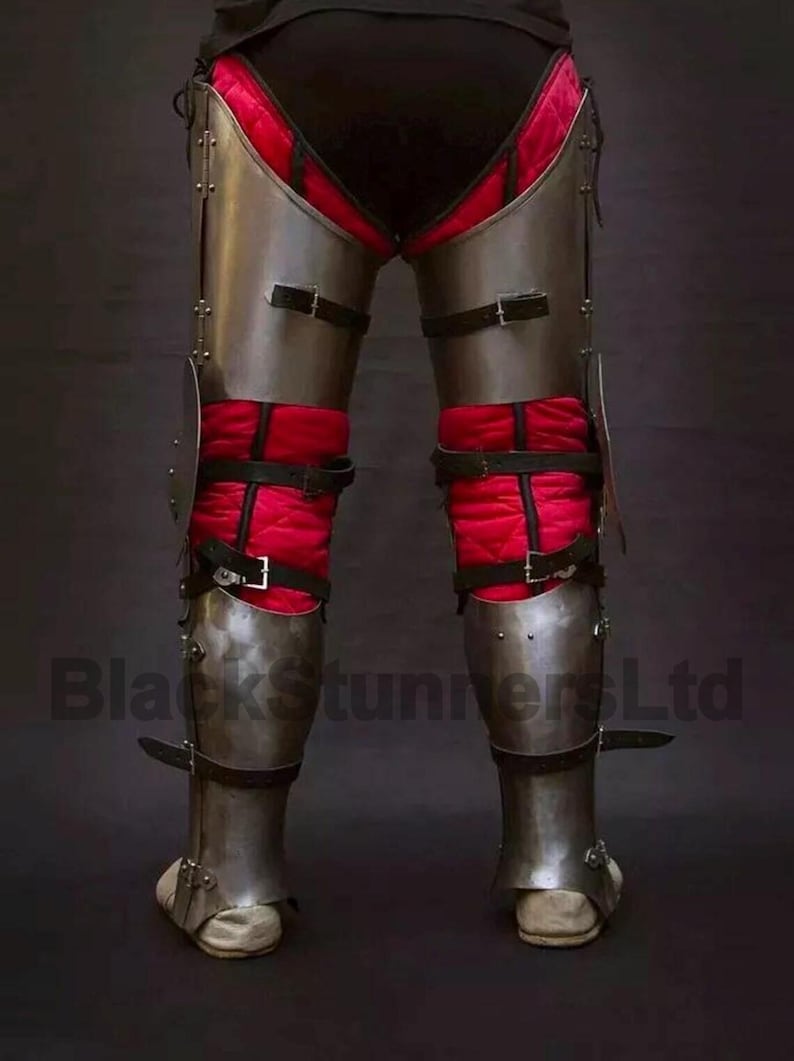 May include: Steel leg armor with black leather straps and red quilted padding. The armor is designed to protect the legs and feet. The image shows the lower body of a person wearing the armor. The text "BlackStunnersLtd" is visible.
