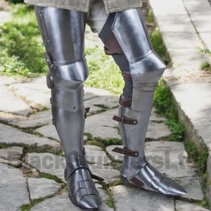 May include: Polished steel leg armor, featuring articulated plates for flexibility and protection. The armor includes knee and shin guards, secured with leather straps and buckles. The design is historically accurate, reflecting medieval craftsmanship.