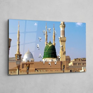 May include: A rectangular wall clock featuring a detailed image of a mosque with a green dome and multiple minarets against a blue sky. The clock face displays Arabic numerals. The clock hands are visible.