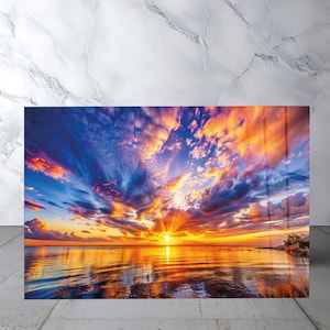 Può includere: Una stampa artistica da parete rettangolare che raffigura un vivace tramonto sopra uno specchio d'acqua calmo. Il cielo è pieno di nuvole drammatiche nei toni del blu profondo, arancione brillante e giallo, con il sole riflesso sull'acqua.