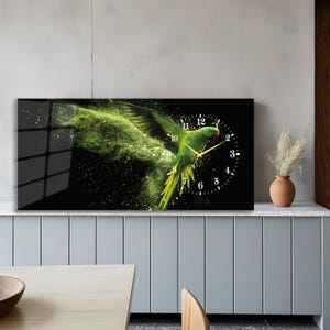 Puede incluir: Un reloj de pared rectangular con un loro verde vibrante en vuelo sobre un fondo negro. La esfera del reloj es blanca con números negros y manecillas doradas. El loro está rodeado por un efecto verde similar a una nube.