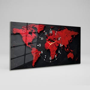 Op de afbeelding: Rechthoekige wandklok met een rood wereldkaartontwerp op een zwarte achtergrond. De klok heeft een zwarte wijzerplaat met witte cijfers en gouden wijzers. Een decoratief item.
