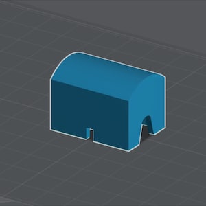 May include: A three-dimensional blue block with a rounded top surface, featuring a rectangular cutout in the center of the front face and a larger arched opening on the right side, presented in an isometric view against a dark gray grid background.
