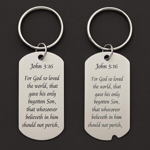 Puede incluir: Dos llaveros plateados con diseño de chapa de identificación. Cada etiqueta tiene el texto "John 3:16" y un versículo religioso. Los llaveros tienen un anillo circular para sujetar llaves.