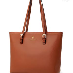 May include: A brown leather tote bag with two handles. The bag has gold-colored buckles and the text "Kelly Paradise" is printed on the front. The word "IMPORTED" is printed at the bottom.