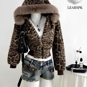 May include: A mannequin displays a leopard print jacket with a fur-trimmed hood and denim shorts. The jacket has a zipper closure and brown cuffs. A black purse hangs from the mannequin's shoulder. The shorts have a brown belt. A sign says "LUXURY SALE 50% OFF" and "LEARSPK".