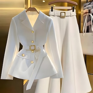 May include: A white two-piece suit comprising a blazer with gold buttons and a matching belt, alongside wide-leg trousers. The blazer has an asymmetrical design. The text "LEAR" and "IMPORTED LEARSPK" are visible.