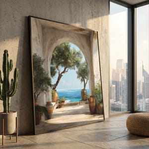 Pode incluir: Uma grande obra de arte emoldurada retratando uma porta arqueada com vista para uma cena costeira com árvores, plantas em vasos e o mar. A obra de arte está encostada em uma parede de concreto, com um cacto em um vaso à esquerda e uma vista da cidade através de uma janela.