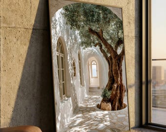 May include: A rectangular framed wall art print depicting a sunlit Mediterranean-style corridor with white textured walls, arched windows, and a stone-paved floor. A large, gnarled olive tree stands in the foreground, casting shadows across the path.