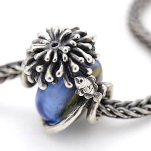 May include: A sterling silver charm bead featuring a detailed sea anemone top and a small fish figure attached to the side. The bead is threaded onto a silver chain and contains a smooth, rounded blue and green glass core element.