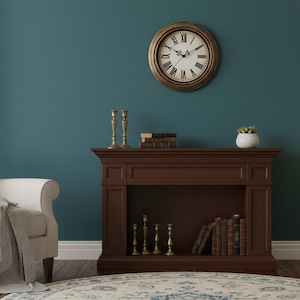 May include: A cozy living room scene featuring a cream-colored armchair with a blanket, a dark brown fireplace, and a gold-framed clock. A floor lamp with a beige shade and a patterned rug complete the elegant decor.