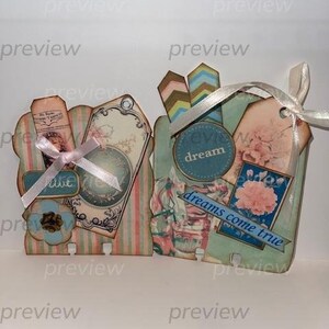 Könnte beinhalten: Ein Set aus vier dekorativen Etiketten im Vintage-Stil. Die Etiketten sind aus Papier und zeigen verschiedene Designs, darunter Blumen, Streifen und eine fantasievolle Illustration eines Mädchens. Die Etiketten sind mit einem weißen Band zusammengebunden und haben den Text "believe dream dreams come true" aufgedruckt.