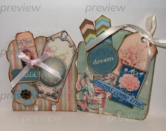 Könnte beinhalten: Ein Set aus vier dekorativen Etiketten im Vintage-Stil. Die Etiketten sind aus Papier und zeigen verschiedene Designs, darunter Blumen, Streifen und eine fantasievolle Illustration eines Mädchens. Die Etiketten sind mit einem weißen Band zusammengebunden und haben den Text "believe dream dreams come true" aufgedruckt.