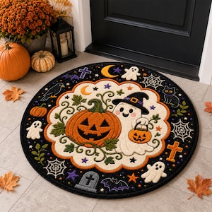 May include: A round black rug featuring a central cream-coloured scalloped border enclosing a large orange jack-o'-lantern and a white ghost wearing a witch hat. The surrounding black border displays small ghosts, bats, spiders, webs, and crosses.