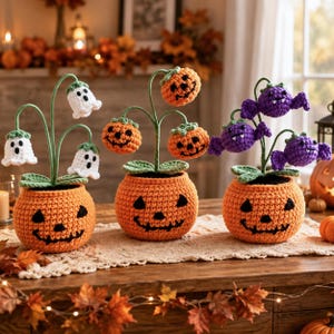 Puede incluir: Tres decoraciones de Halloween tejidas a ganchillo en macetas naranjas con forma de calabaza. La primera maceta contiene flores de fantasma blancas, la segunda flores de calabaza naranjas y la tercera flores de murciélago moradas.