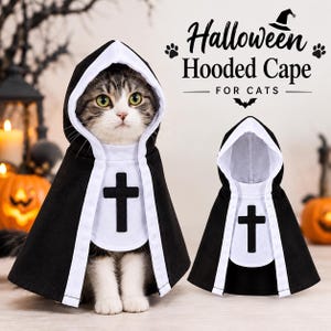 May include: A black hooded cape for cats with a white trim and a black cross emblem on the chest. The text Halloween Hooded Cape FOR CATS is visible in the upper right corner. The cape features a hood and a front panel design.