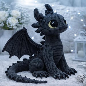 Peut inclure: Une peluche dragon au crochet gris foncé avec de grands yeux noirs aux iris jaunes, des oreilles pointues, une longue queue et des ailes texturées. La créature présente de petites pointes le long du dos et de la queue, avec des griffes noires.