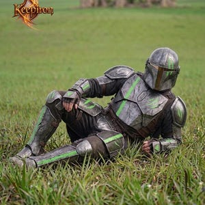 Puede incluir: Una persona con una armadura detallada, gris met&aacute;lico y verde, casco y guantes, descansando en un campo de hierba. La armadura tiene detalles en verde y est&aacute; dise&ntilde;ada con detalles intrincados. El logotipo "Keepiron" es visible en la esquina superior izquierda.