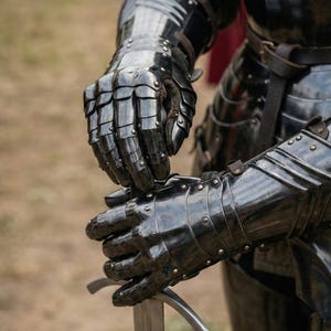 May include: Close-up of black, articulated knight's armor, including gauntlets and a portion of the chest and arm protection. The gauntlets are holding a silver sword. The armor has a reflective, polished surface.