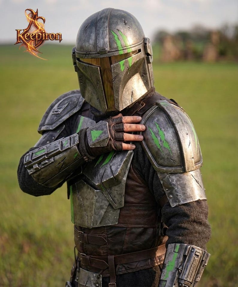 Puede incluir: Casco y armadura mandalorianos detallados en tonos grises, marrones y verdes. La armadura presenta detalles desgastados por la batalla y acentos verdes. El logotipo de Keepiron es visible en la esquina superior izquierda. El tema general es cosplay y ciencia ficci&oacute;n.