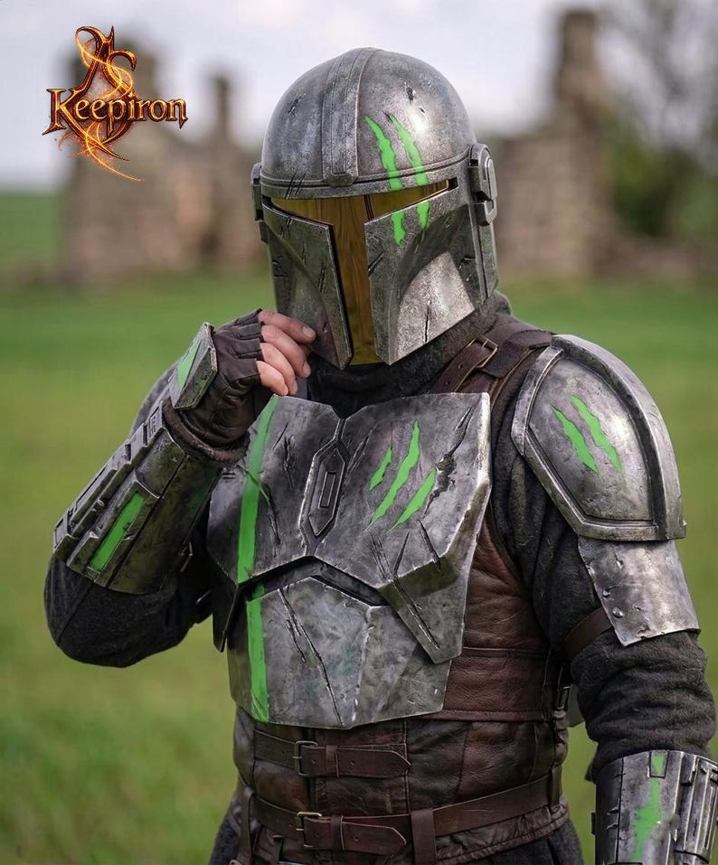 Puede incluir: Un casco y una armadura de metal desgastado con detalles verdes. El casco tiene una visera en forma de T y la armadura presenta marcas de ara&ntilde;azos. El logotipo "Keepiron" est&aacute; en la esquina superior izquierda.