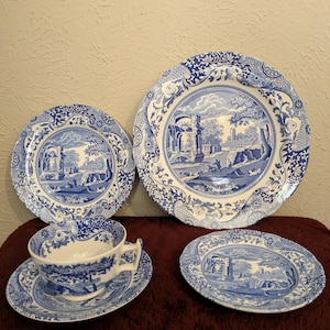 May include: A collection of blue and white ceramic tableware featuring a scenic landscape design. The set includes a teacup and saucer, along with plates of varying sizes. The plates and cup have a detailed border design.
